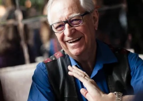 image of a mature gentleman with grey hair and glasses wearing a shirt and waistcoat and who is smiling and laughing