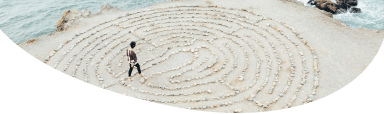 Image of a person standing on a beach walking through a maze made of lines on the sand