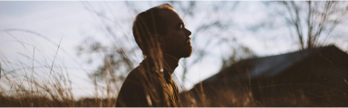 Silhouette of a male immersed in nature, looking into the distance and reflecting, whilst standing next to trees