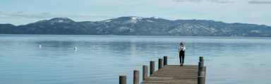 image of someone standing alone at the end of a jetty looking out onto a lake