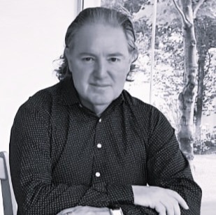 Godfrey O'Flaherty, CEO of IIRFL and Global Custodian of Radical Forgiveness sitting at a desk, wearing a smart dark shirt