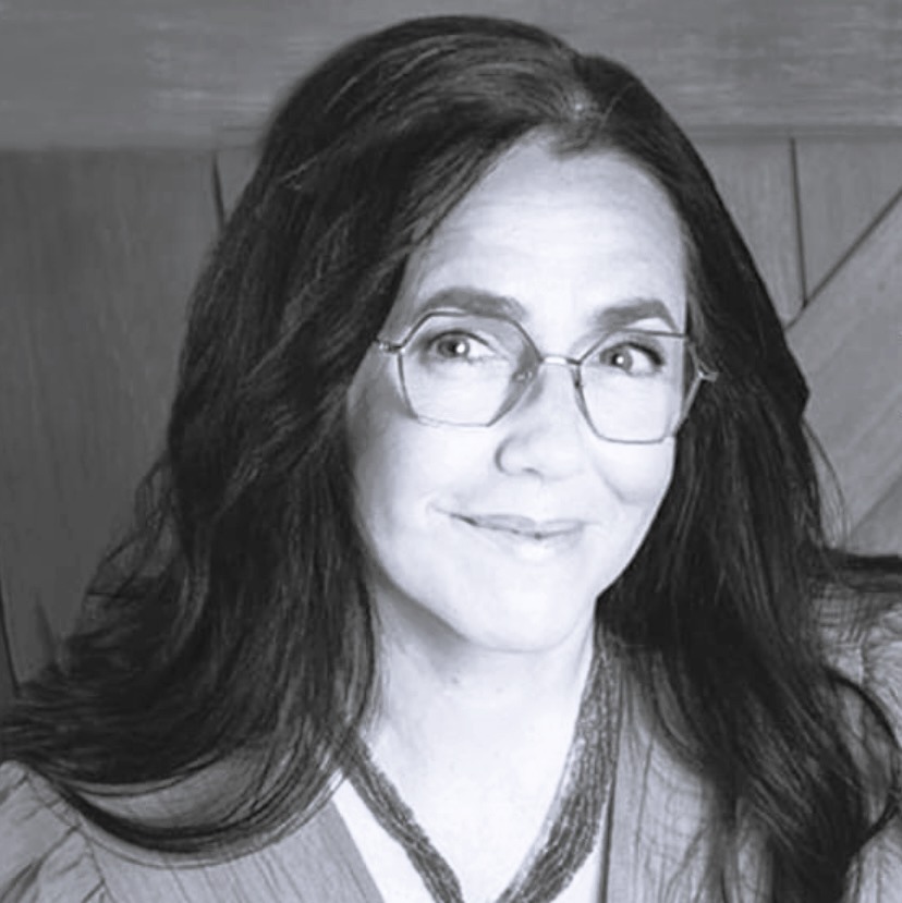 Black and white headshot of a woman with long dark hair, wearing glasses, looking directly at the camera.