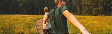 image of a male walking through a field behind another person and reaching backwards for the person behind him