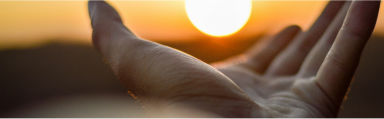 A hand reaching out towards the orange sky, as if holding the setting sun