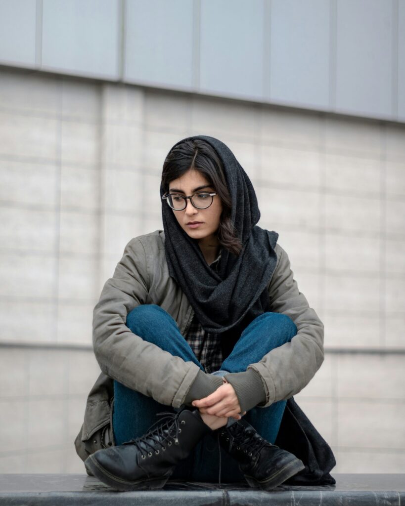 A young Muslim girl wearing a scarf loosely around her head and casual clothing and looking deep in thought